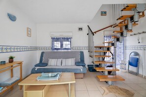 Una sala de estar con sofá, una mesa, una escalera y vistas al exterior.