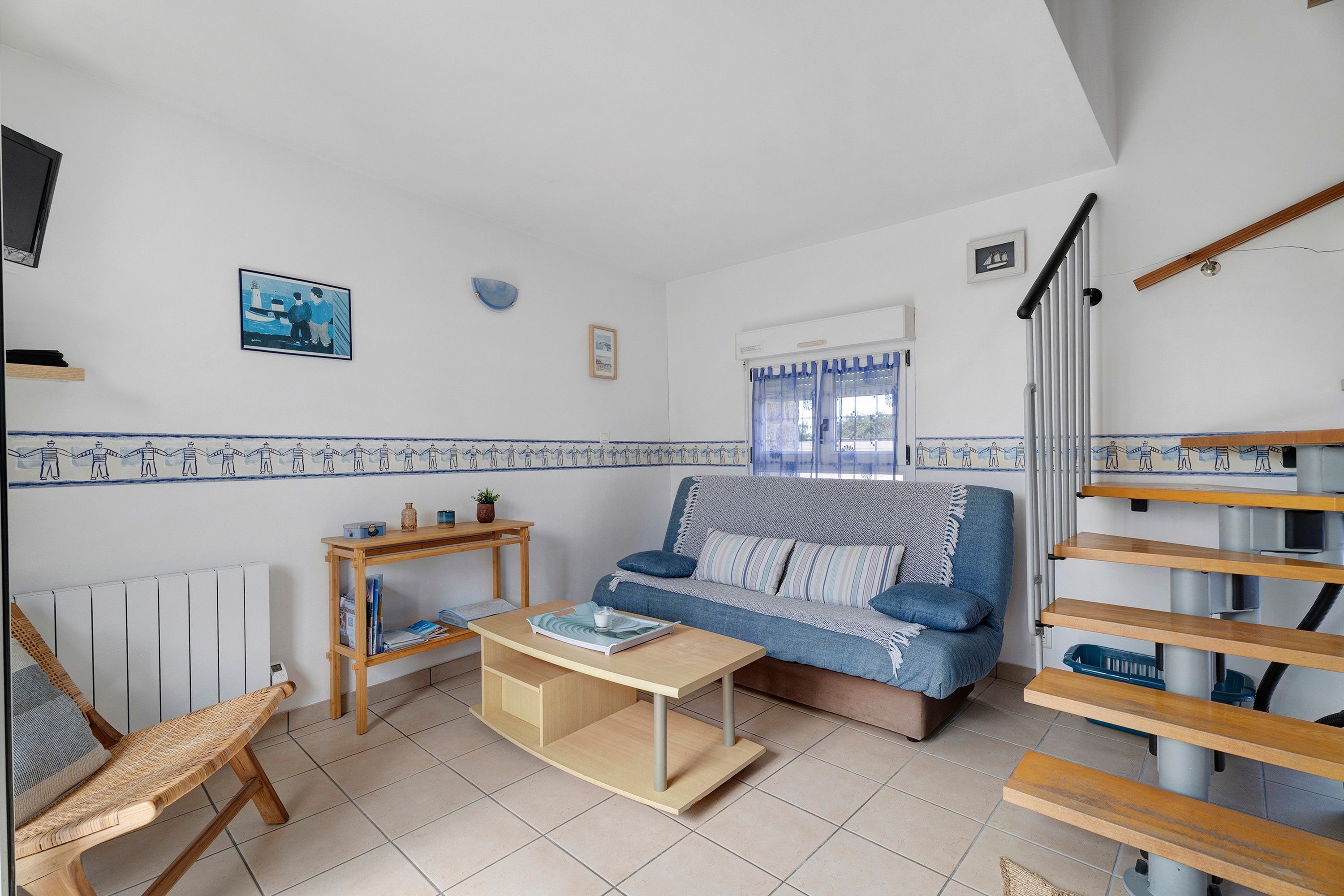 Una sala de estar con un sofá, una mesa de centro, una mesita de madera, un sillón de mimbre y una escalera.