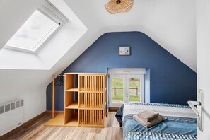 Ein Schlafzimmer mit schrägverdeckelter Decke, Dachfenster, Bett, Kleiderschrank und Fenster.
