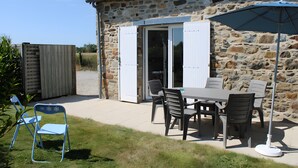 A stone building with a patio area featuring a table and chairs, a folding chair, and a large umbrella. - Gîte ti glas - Les Gîtes de la Cour Chevalier (La Fresnais)
