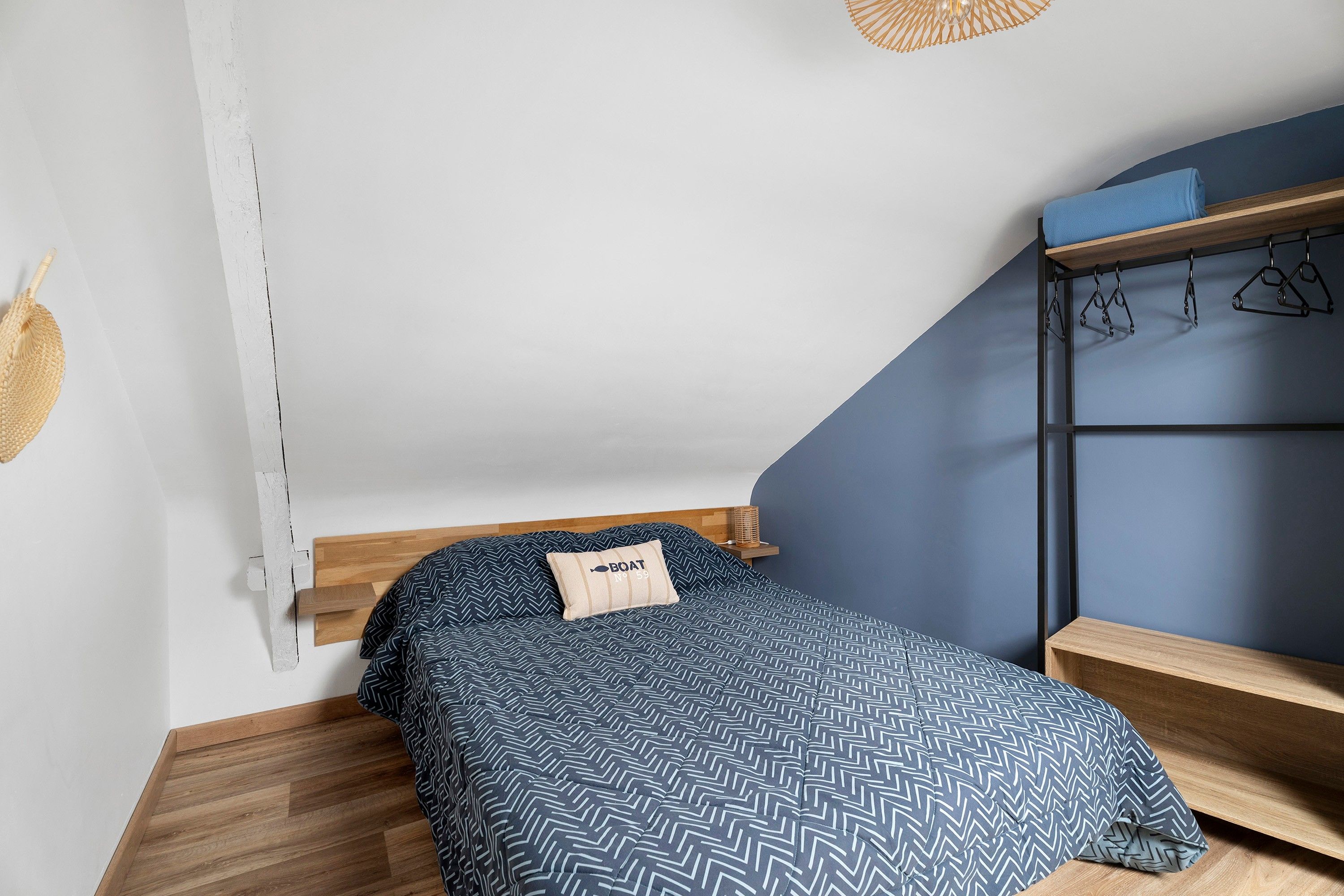 A bedroom with a bed, a wooden headboard, a blue wall, and a small shelf with a basket.