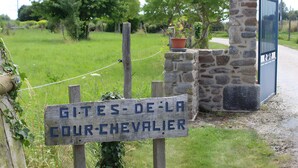A rustic wooden sign with text, a stone wall, a potted plant, and a metal gate. - Gîte ti glas - Les Gîtes de la Cour Chevalier (La Fresnais)