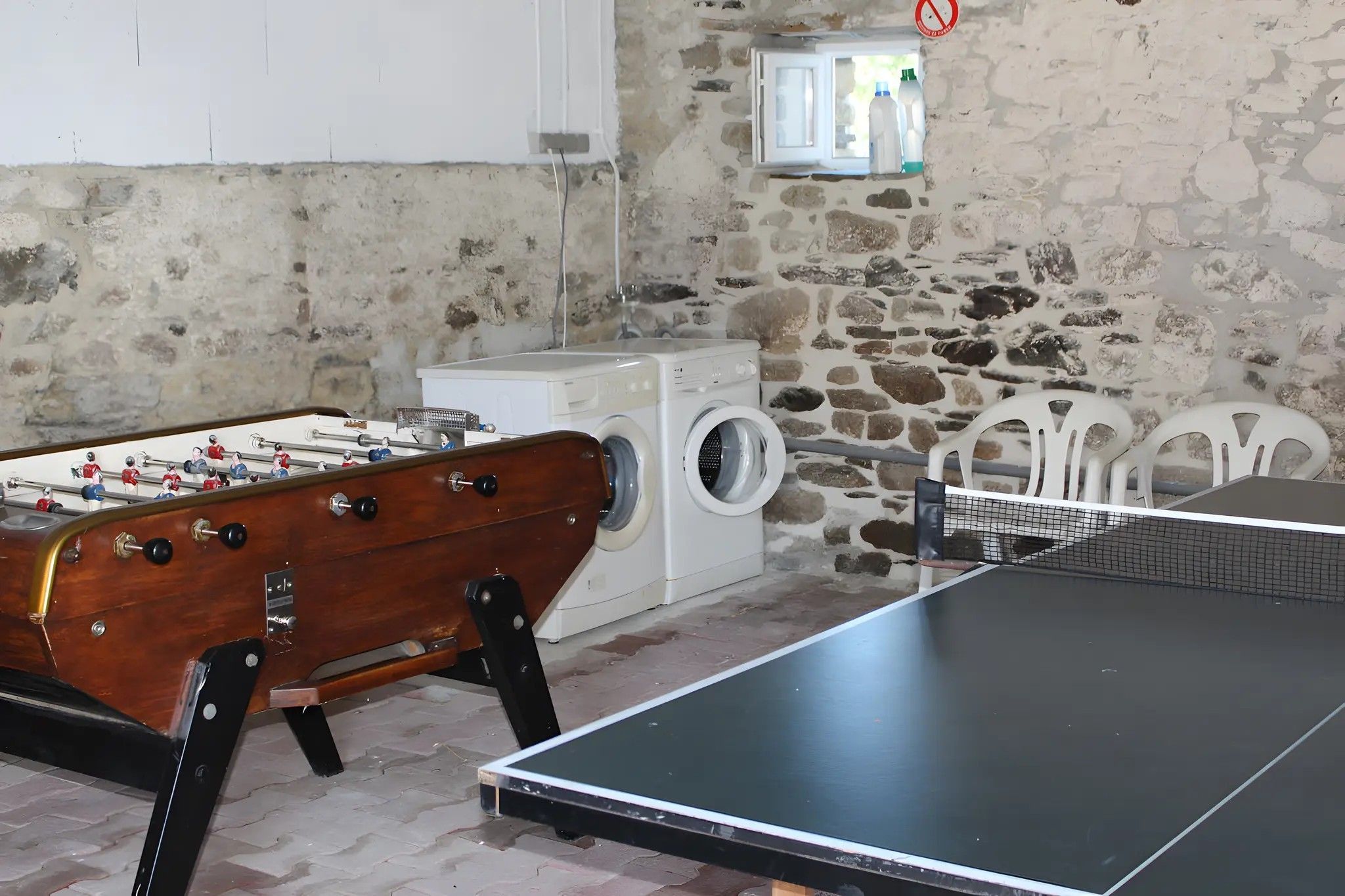 Ein Zimmer mit Tischfußballtisch, Waschmaschine, Tischtennisplatte und einer Steinwand.