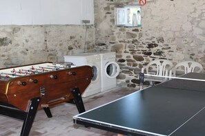 Una habitación con mesa de futbolín, lavadora, mesa de ping pong y pared de piedra.