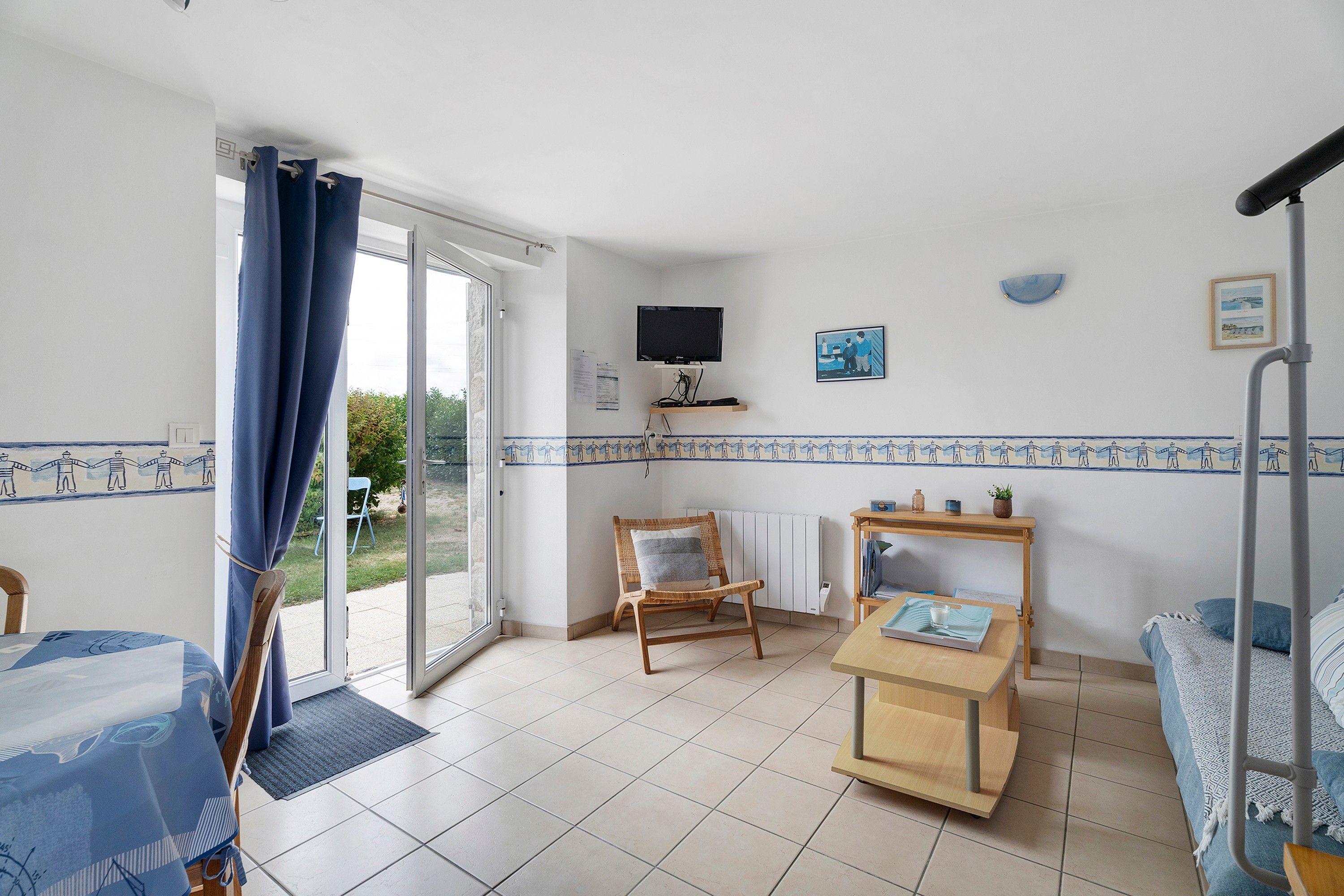 A room with a bed, a chair, a table, a TV, and a window with curtains.