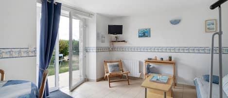 A room with a bed, a chair, a table, a TV, and a window with curtains.
