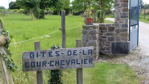 Ein rustikales Holzschild mit Schriftzug, eine Steinsäule, ein Blumentopf und ein Metalltor.
