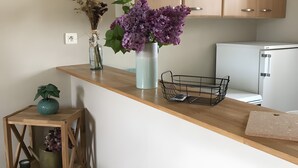 Eine Küche mit Holdekor, einer weißen Arbeitsplatte, einer Vase mit violetten Blumen, einem kleinen Holztisch mit einer Pflanze und einem Metallkorb.