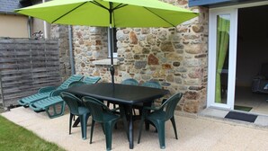 Eine Terrasse mit Tisch und Stühlen, einem grünen Sonnenschirm und einer Steinmauer.