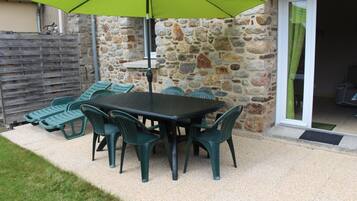 Une terrasse avec une table et des chaises, un parasol vert et un mur en pierre.