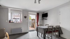 A dining area with a table and chairs, a television mounted on the wall, and a window with a curtain.