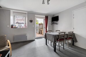 A dining area with a table and chairs, a television mounted on the wall, and a window with a curtain.