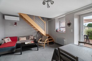 Ein modernes Wohnzimmer mit Holztreppe, grauem Sofa und einem Essbereich mit Tisch.