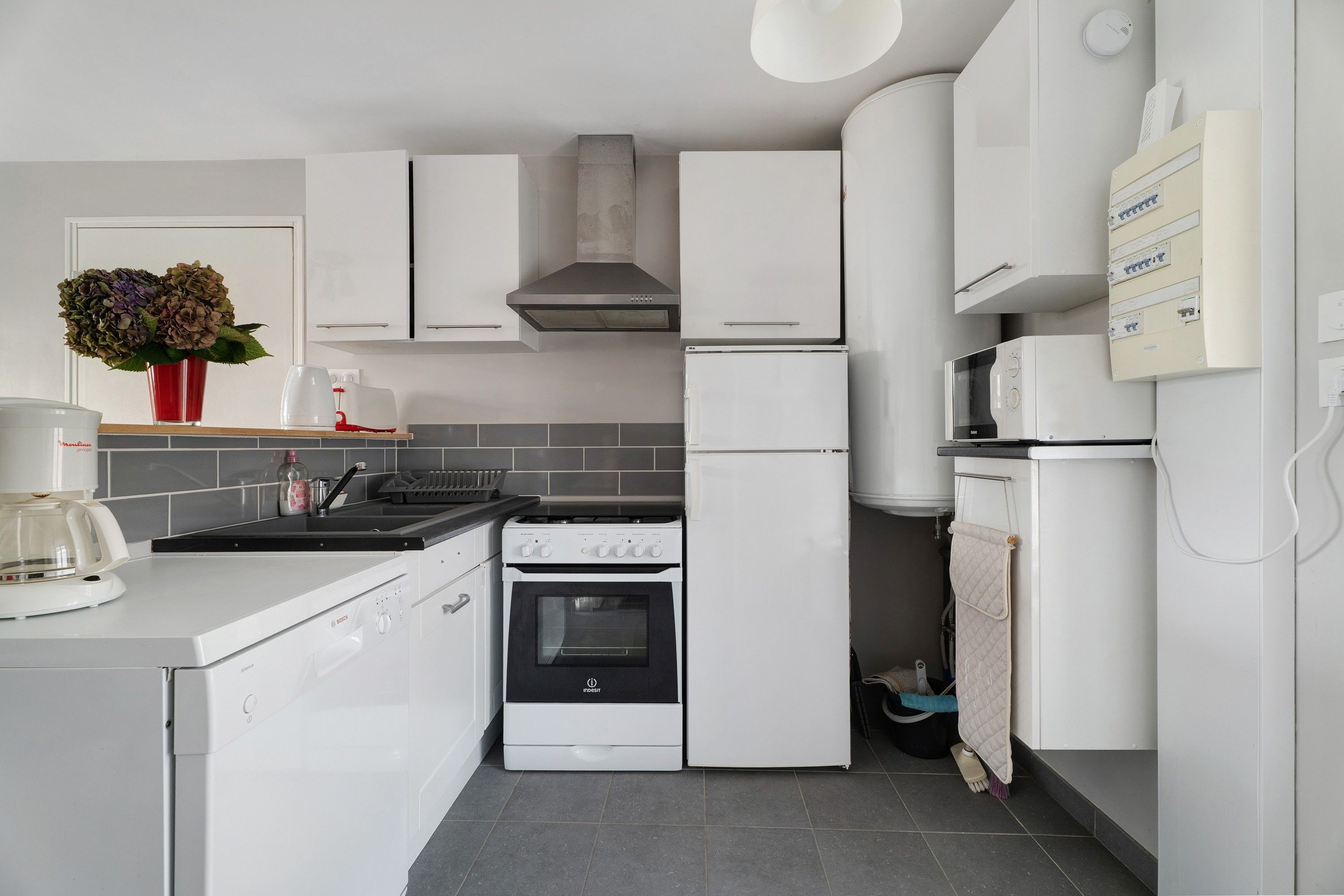 Une cuisine moderne avec des meubles blancs, un lave-vaisselle Bosch, un four Indesit et un four à micro-ondes Siemens.
