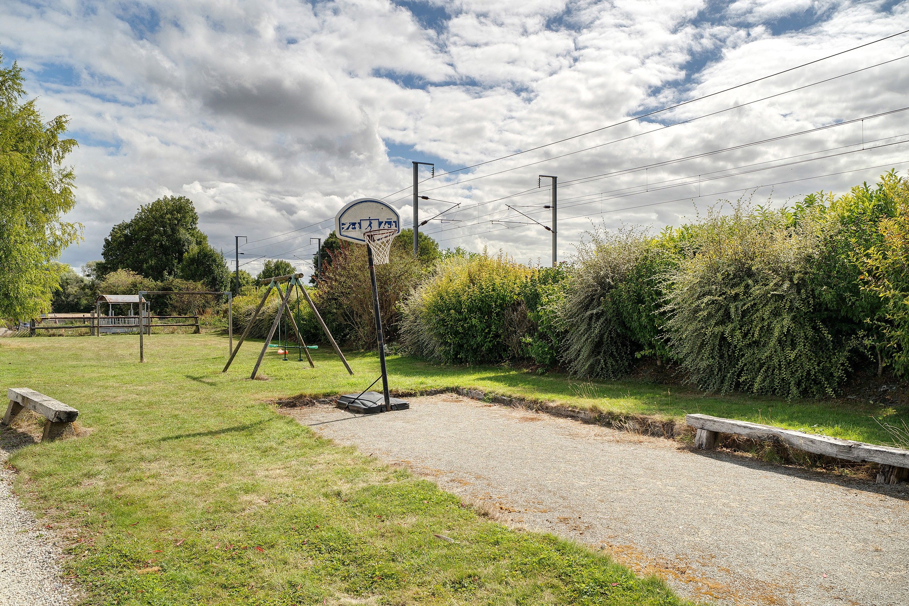Ein Basketballplatz mit Korb, umgeben von Grünflächen und einem Kiesweg.