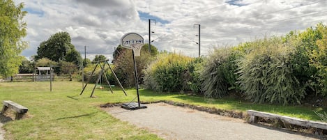 Ein Basketballplatz mit Korb, umgeben von Grünflächen und einem Kiesweg.