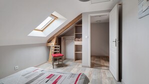 A bedroom with a sloped ceiling, a skylight, a bed, a chair, and a wardrobe.