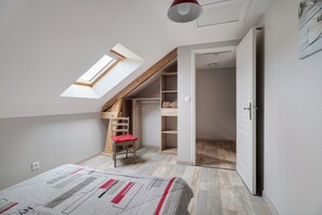 A bedroom with a sloped ceiling, a skylight, a bed, a chair, and a wardrobe.