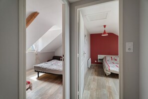 A bedroom with a sloped ceiling, a bed with a patterned bedspread, a red wall, and a red ceiling light.