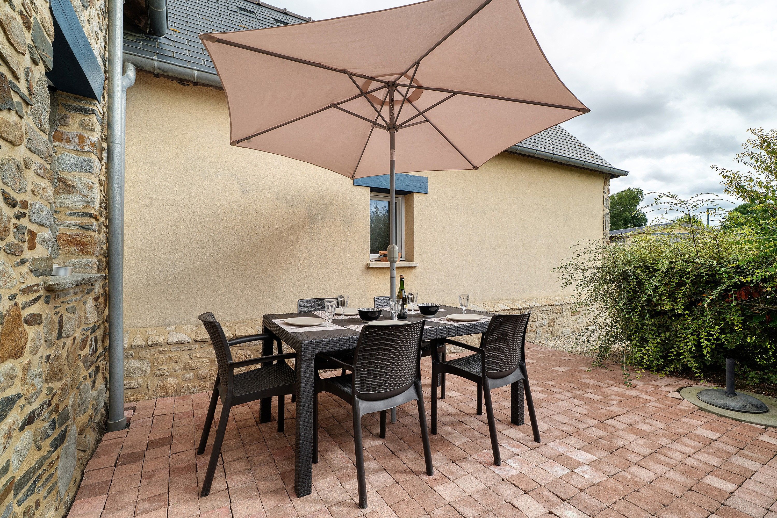 An outdoor patio with a table and chairs, a large umbrella, and a stone wall.