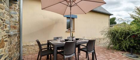 An outdoor patio with a table and chairs, a large umbrella, and a stone wall.