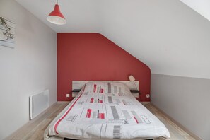 Un dormitorio con techo inclinado, una cama con colcha estampada, pared roja y radiador blanco.