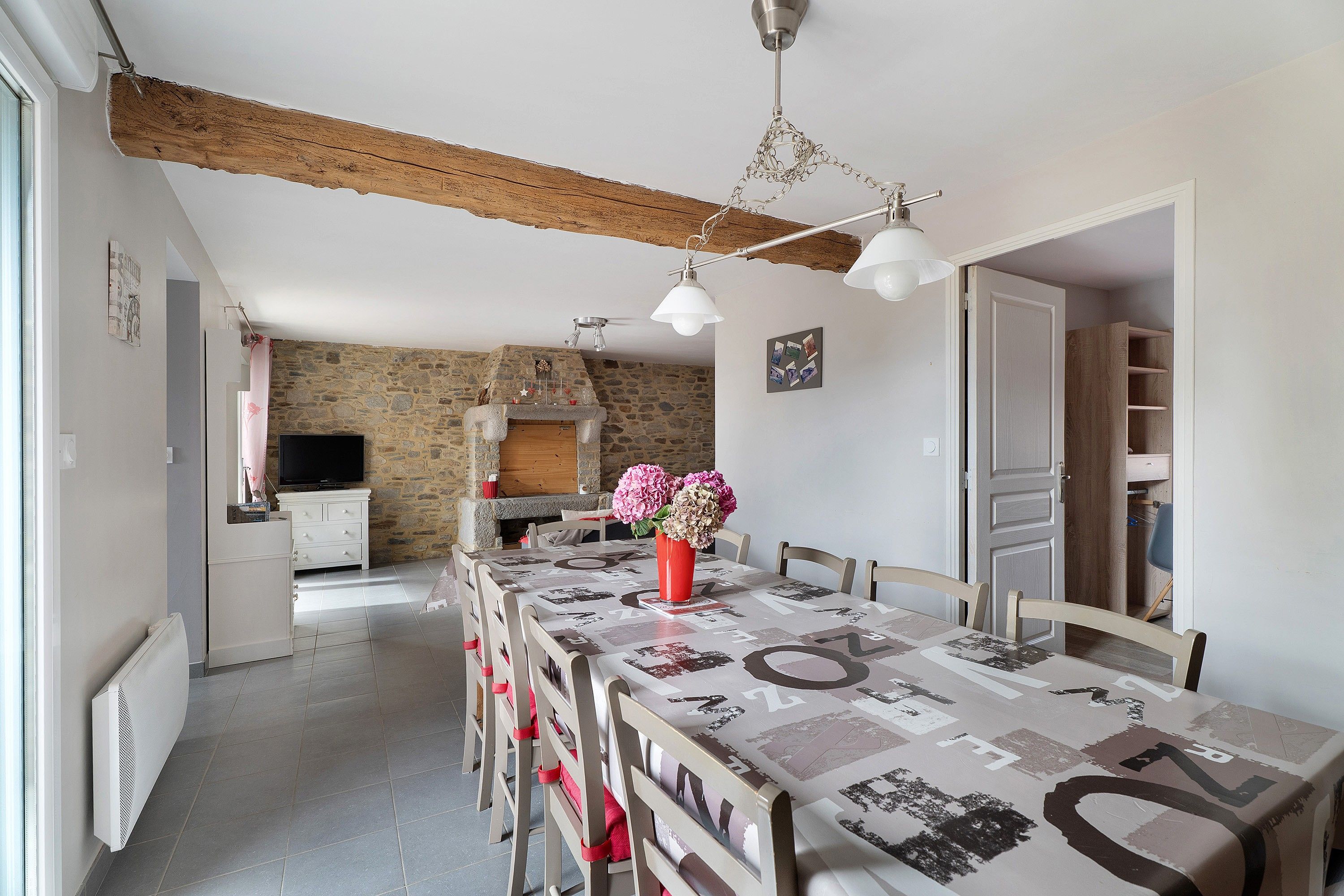 Un comedor con una larga mesa, sillas, un jarrón con flores y una pared de piedra al fondo.