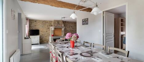 Un comedor con una larga mesa, sillas, un jarrón con flores y una pared de piedra al fondo.