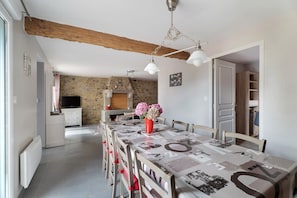 Un espace repas avec une longue table, des chaises, un vase rempli de fleurs et, en arrière-plan, un mur en pierre.