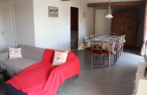A living room with a sofa, a dining table with chairs, a wooden cabinet, and a tiled floor.