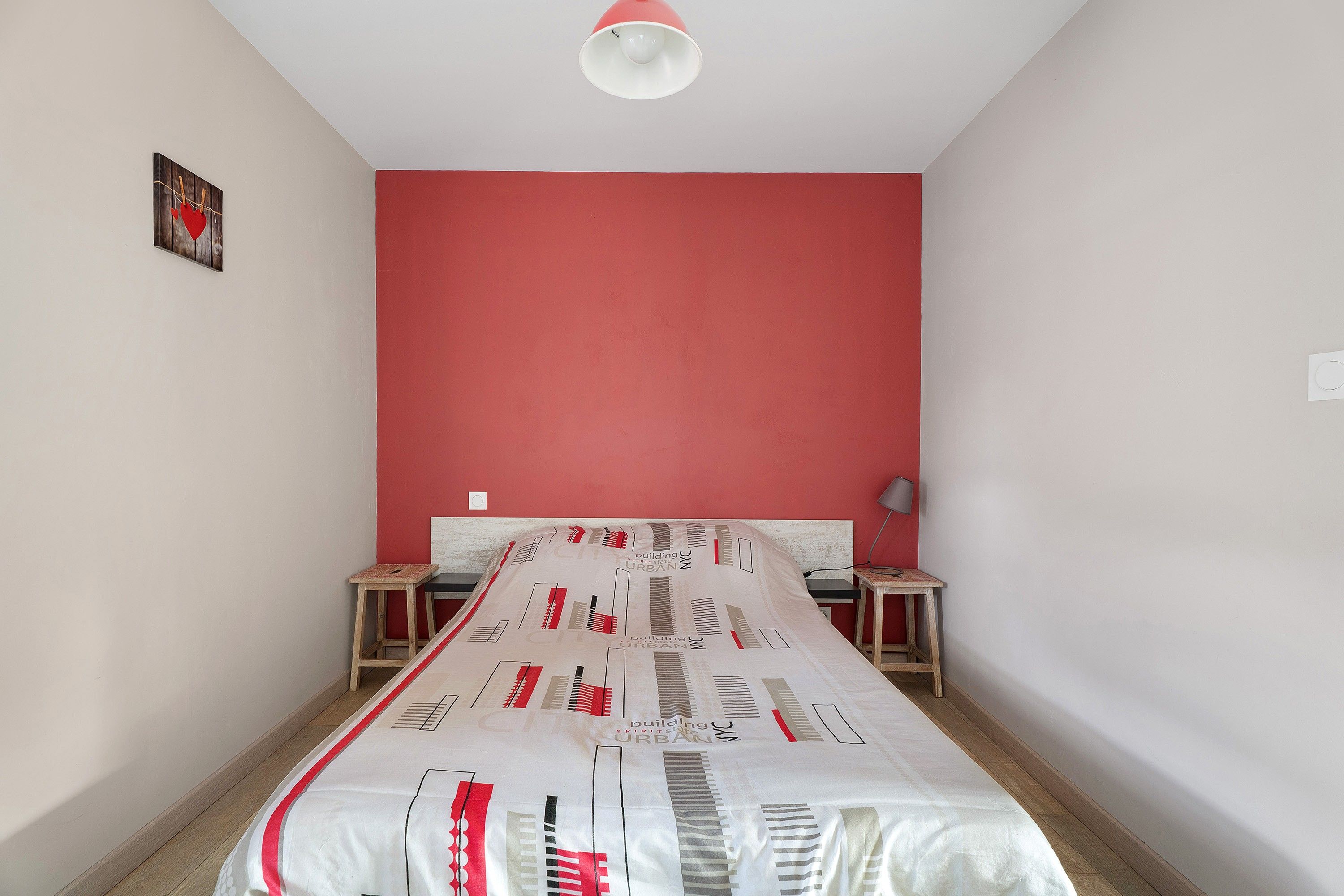 A room with a bed, two nightstands, a red wall, and a ceiling light.