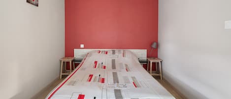 A room with a bed, two nightstands, a red wall, and a ceiling light.