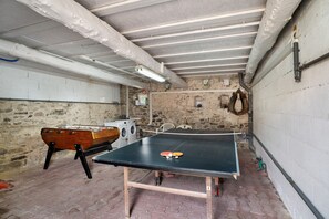 A room with a ping pong table, washing machine, and a foosball table.