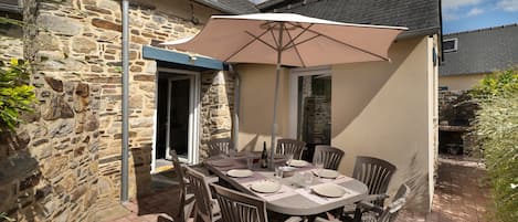 An outdoor patio with a stone wall, a table set for four, and a large umbrella providing shade.