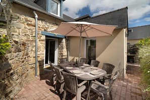 Une terrasse extérieure avec un mur en pierre, une table dressée pour quatre personnes et un grand parasol offrant de l’ombre.