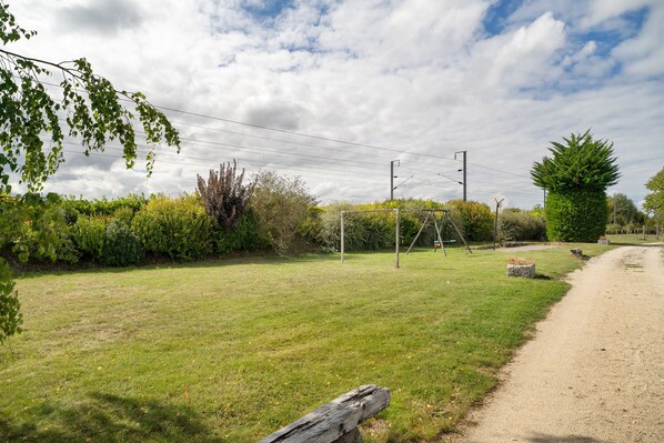A grassy area with a dirt path, surrounded by trees and shrubs.