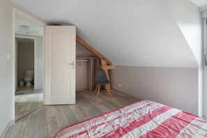 Une chambre avec un plafond en pente, une chaise en bois, un lit recouvert d’une couverture à motifs et un placard avec une tringle à vêtements.