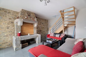 A living room with a stone fireplace, a wooden staircase, and a sofa with a red throw.