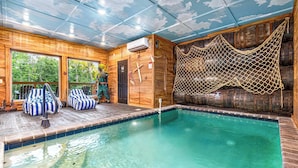 Una cabaña de madera con piscina, sillones de mimbre a rayas y una zona con mosquitero.