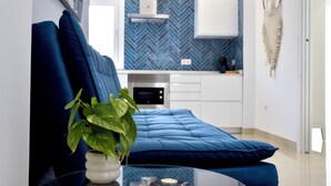 A modern living room with a blue sofa, a glass coffee table, and a potted plant.