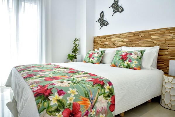 A neatly made bed with a floral bedspread, a wooden headboard, and a bedside table with a geometric-patterned nightstand.