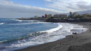 A beach with waves, people, and buildings in the background.