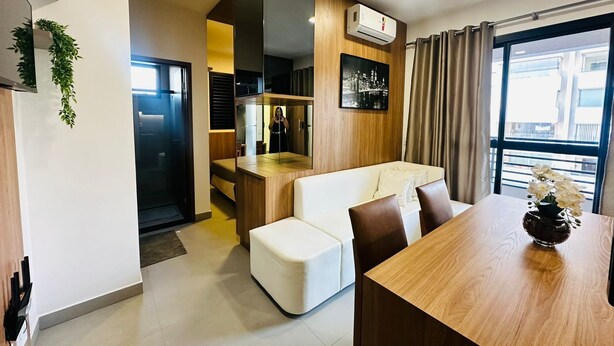 Eine moderne Wohnung mit Essbereich, einem weißen Sofa, einem Holzesstisch und einer Küche mit integriertem Backofen und einem fenster mit Vorhängen.