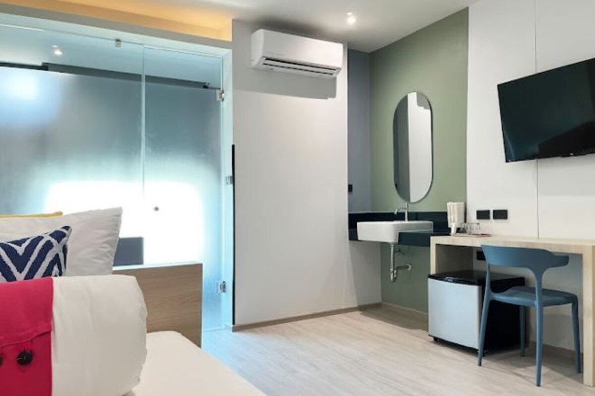 Una habitación de hotel moderna con cama, escritorio, silla, televisor y aire acondicionado.
