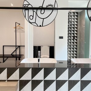 Un baño moderno con encimera a cuadros blancos y negros, un lavamanos blanco y una zona de ducha con diseño de mosaicos geométricos.
