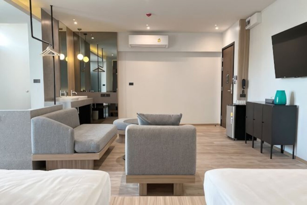 A modern hotel room with a sofa, a small table, a bed, a TV, and a wardrobe.