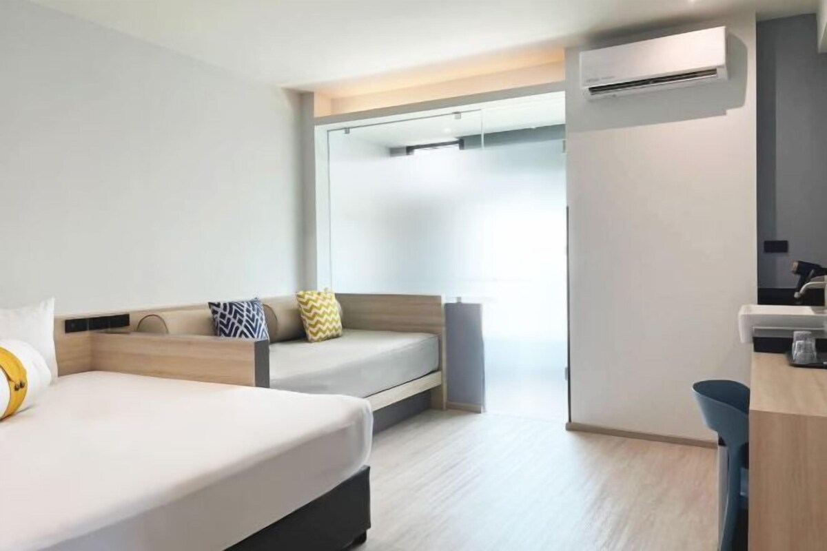 Una habitación de hotel moderna con dos camas, una kitchenette pequeña y una puerta corredera que da a un baño.