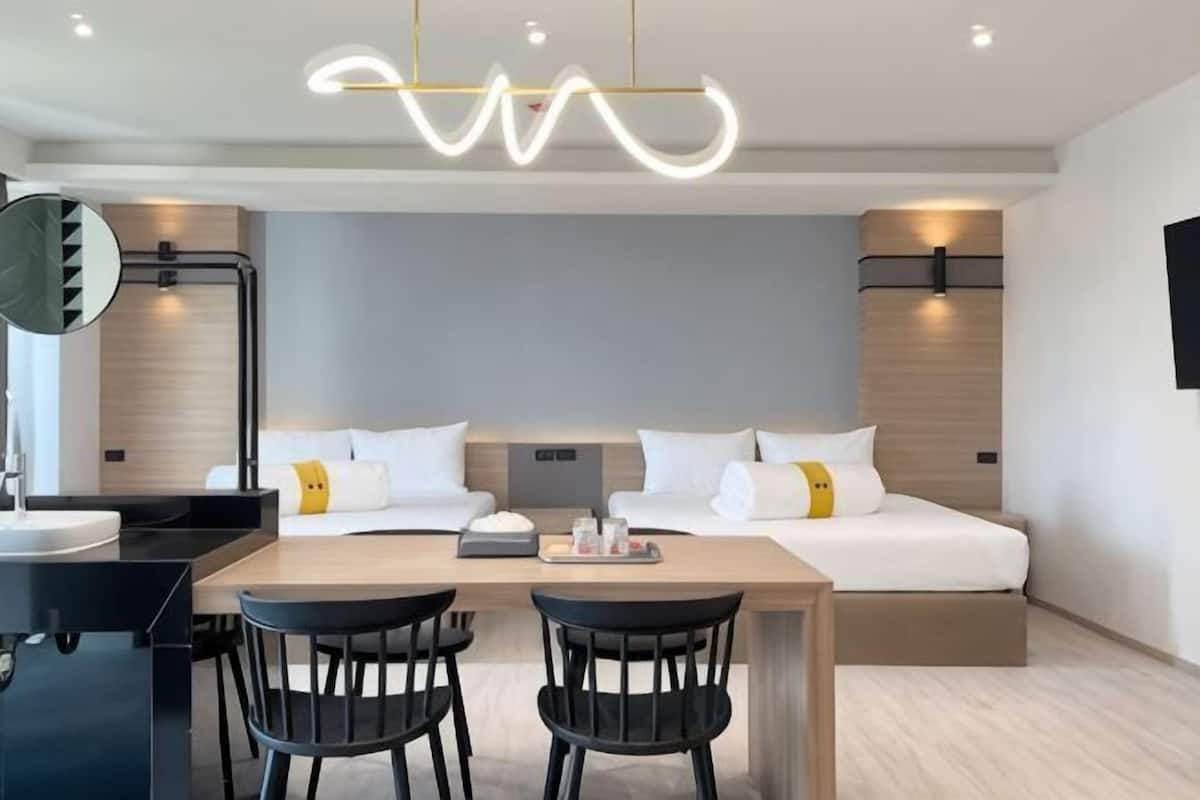Une chambre d’hôtel moderne équipée d’un lit, de tables de chevet, d’un bureau avec des chaises et d’un grand miroir.