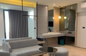 Un baño moderno con tocador doble lavabo, cabina de ducha con mampara de vidrio y zona de estar con sofá y mesa redonda.