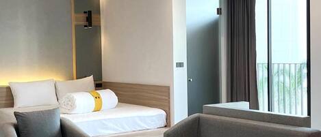 Una habitación de hotel moderna con una cama, dos sofás, una mesita y un balcón con cortinas.